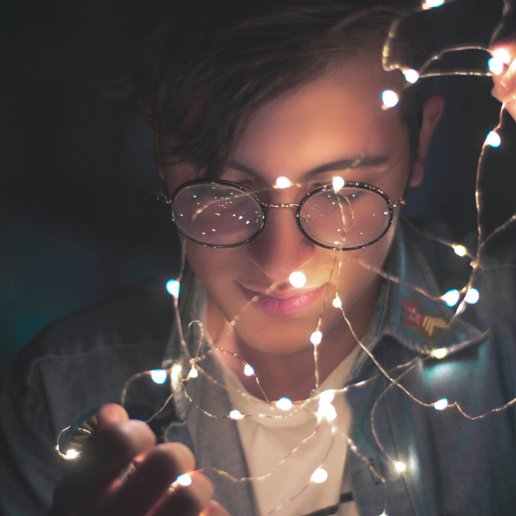 Young man with glasses illuminated by fairy lights, creating a stylish and artistic portrait.